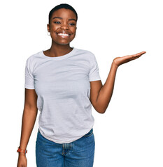 Sticker - Young african american woman wearing casual white t shirt smiling cheerful presenting and pointing with palm of hand looking at the camera.