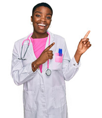 Canvas Print - Young african american woman wearing doctor uniform and stethoscope smiling and looking at the camera pointing with two hands and fingers to the side.