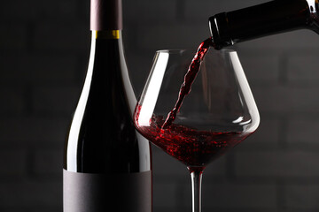 Sticker - Pouring red wine into glass and bottles against brick wall background, closeup