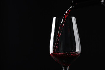 Sticker - Pouring red wine into glass against black background, closeup. Space for text