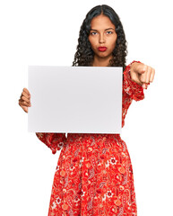 Sticker - Young african american girl holding blank empty banner pointing with finger to the camera and to you, confident gesture looking serious