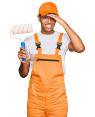 Poster - Young handsome african american man wearing cap and painter clothes holding painting roll stressed and frustrated with hand on head, surprised and angry face