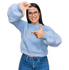 Wall Mural - Young hispanic woman wearing casual clothes and glasses smiling making frame with hands and fingers with happy face. creativity and photography concept.