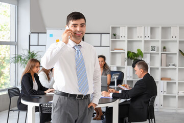 Canvas Print - Young businessman talking by mobile phone at meeting in office