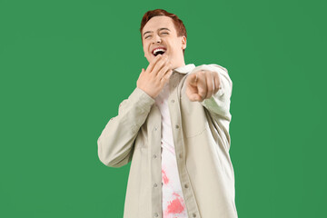 Wall Mural - Laughing young man pointing at viewer on green background. Accusation concept