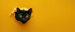 A striking black cat with captivating eyes peeks out from a torn yellow paper background