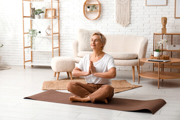 Poster - Mature woman meditating while sitting on floor at home