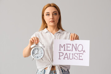 Poster - Mature woman holding paper with word MENOPAUSE and alarm clock on light background