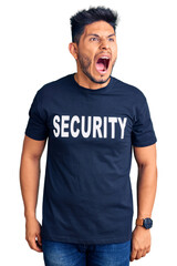 Wall Mural - Handsome latin american young man wearing security t shirt angry and mad screaming frustrated and furious, shouting with anger. rage and aggressive concept.