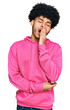 Young african american man with afro hair wearing casual pink sweatshirt bored yawning tired covering mouth with hand. restless and sleepiness.
