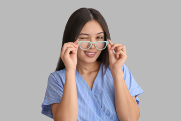 Wall Mural - Beautiful young happy Asian woman with new eyeglasses on grey background