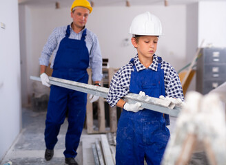 Wall Mural - Young boy in overall carrying metal plank with his father during repair works in apartment.