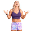 Middle age fit blonde woman wearing sportswear crazy and mad shouting and yelling with aggressive expression and arms raised. frustration concept.