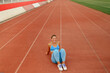 © Zamrznuti tonovi - A sportswoman is sitting on running track at stadium and smiling.