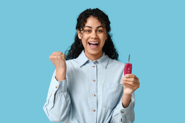 Happy young African-American woman with car key on blue background