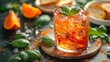   A tight shot of a drink in a glass, adorned with orange peels and basil leaves on the table