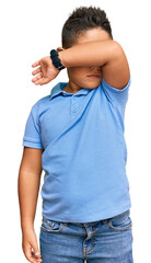 Sticker - Little boy hispanic kid wearing casual clothes covering eyes with arm, looking serious and sad. sightless, hiding and rejection concept