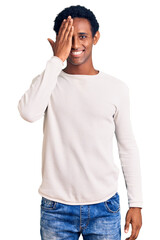 Wall Mural - African handsome man wearing casual winter sweater covering one eye with hand, confident smile on face and surprise emotion.