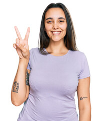 Wall Mural - Young hispanic woman wearing casual clothes smiling with happy face winking at the camera doing victory sign. number two.