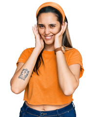 Wall Mural - Young hispanic woman wearing casual clothes covering ears with fingers with annoyed expression for the noise of loud music. deaf concept.