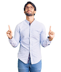 Poster - Handsome hispanic man wearing business shirt and glasses pointing up looking sad and upset, indicating direction with fingers, unhappy and depressed.