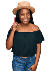 Canvas Print - Young african american woman wearing summer hat pointing finger up with successful idea. exited and happy. number one.