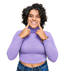 Canvas Print - Young hispanic woman with curly hair wearing casual clothes smiling with open mouth, fingers pointing and forcing cheerful smile