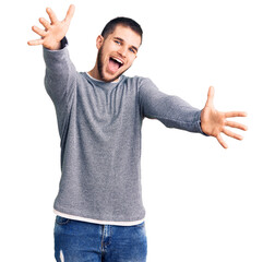 Sticker - Young handsome man wearing casual sweater looking at the camera smiling with open arms for hug. cheerful expression embracing happiness.