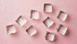 Top view photo of scattered ice cubes and water drops on isolated pastel pink background