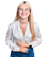 Wall Mural - Beautiful blonde woman wearing elegant shirt and glasses smiling and laughing hard out loud because funny crazy joke with hands on body.