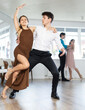 © JackF - Stylish emotional young hispanic guy in white shirt and black trousers enjoying impassioned merengue with female partner wearing elegant dress in latin dance class. Amateur dancing concept
