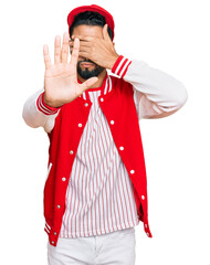 Poster - Young man with beard wearing baseball uniform covering eyes with hands and doing stop gesture with sad and fear expression. embarrassed and negative concept.