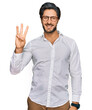 © Krakenimages.com - Young hispanic man wearing business shirt and glasses showing and pointing up with fingers number three while smiling confident and happy.