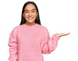 © Krakenimages.com - Young asian woman wearing casual winter sweater smiling cheerful presenting and pointing with palm of hand looking at the camera.
