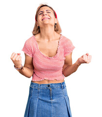 Wall Mural - Young blonde woman wearing casual clothes and diadem very happy and excited doing winner gesture with arms raised, smiling and screaming for success. celebration concept.