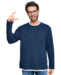 Sticker - Young hispanic man wearing casual clothes and glasses smiling and confident gesturing with hand doing small size sign with fingers looking and the camera. measure concept.