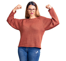 Poster - Beautiful young woman wearing casual clothes and glasses showing arms muscles smiling proud. fitness concept.