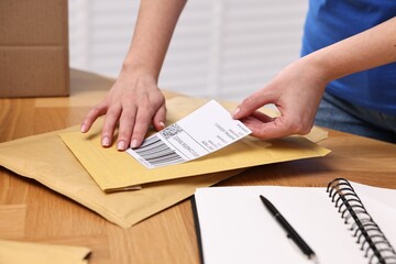 Sticker - Parcel packing. Post office worker sticking barcode on bag at wooden table indoors, closeup