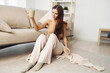 © SHOTPRIME STUDIO - Cozy Morning Bliss: Smiling Woman Holding Coffee Mug, Wrapped in Blanket, Relaxing on Sofa in Warm Autumn Room.