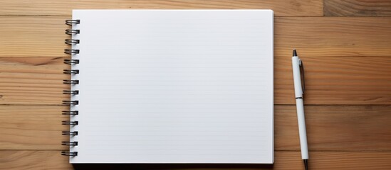 Poster - a white notebook lies open on a wooden table with a pen next to it. the simple setup suggests a spac