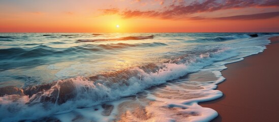 Wall Mural - Golden sun setting on the horizon casting a warm glow over the ocean as waves gently crash on the sandy beach