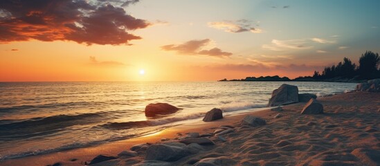 Wall Mural - Vivid sunset along the beach, rocks scattered on the shore with water gently lapping the rocks and sand