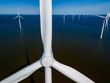 An aerial view of a wind farm featuring rows of windmill turbines gracefully rotating in the vast expanse of the ocean, captured in the Netherlands Flevoland during the vibrant season of Spring.