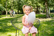 Happy and carefree five-year-old girl sits on a park bench, smiling as she enjoys a large cotton candy.
