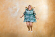 Smiling curvy female model in stylish outfit jumping