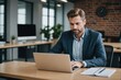 © ThomasLENNE - Businessman working on laptop computer at table in office