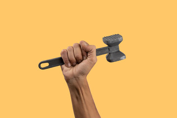 Black male hand holding a kitchen hammer isolated on yellow background