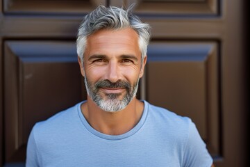 Wall Mural - A man with a beard and gray hair is smiling and wearing a blue shirt