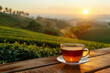 cup of hot tea on wooden table with tea plantation on sunset as background