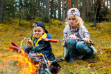 Fototapeta Mapy - children frying sausages on wooden skewers over a bonfire in forest. camping with kids. summer camp